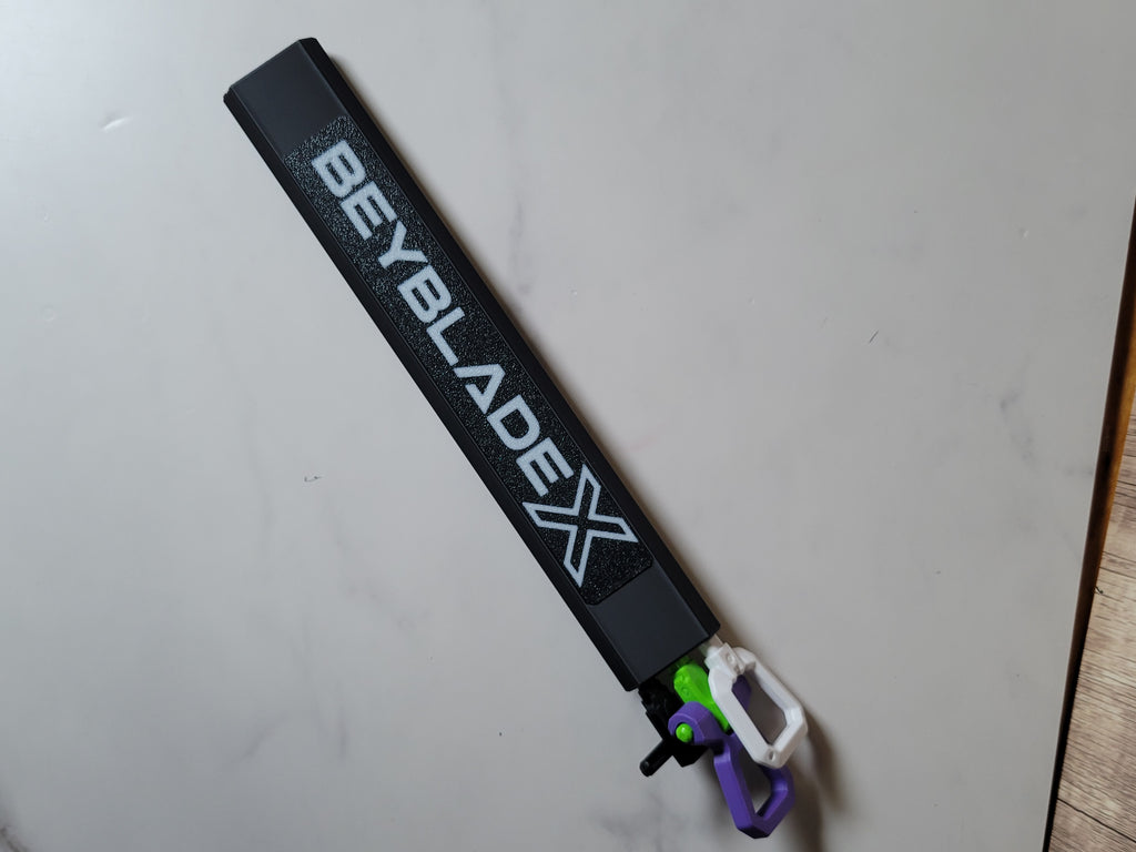 Full view of the black hex rip cord protector with a white Beyblade X logo and three loaded cord handles on a light tabletop.