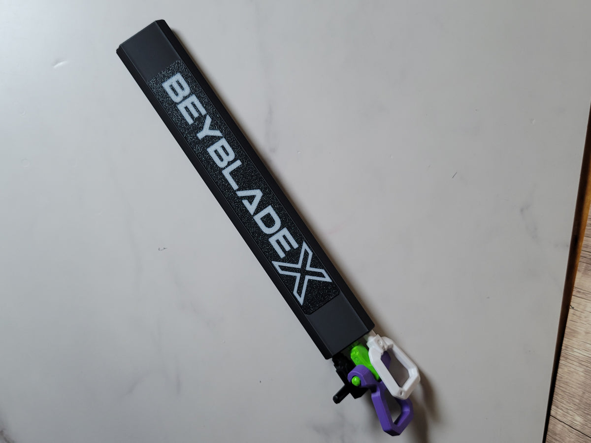 Full view of the black hex rip cord protector with a white Beyblade X logo and three loaded cord handles on a light tabletop.