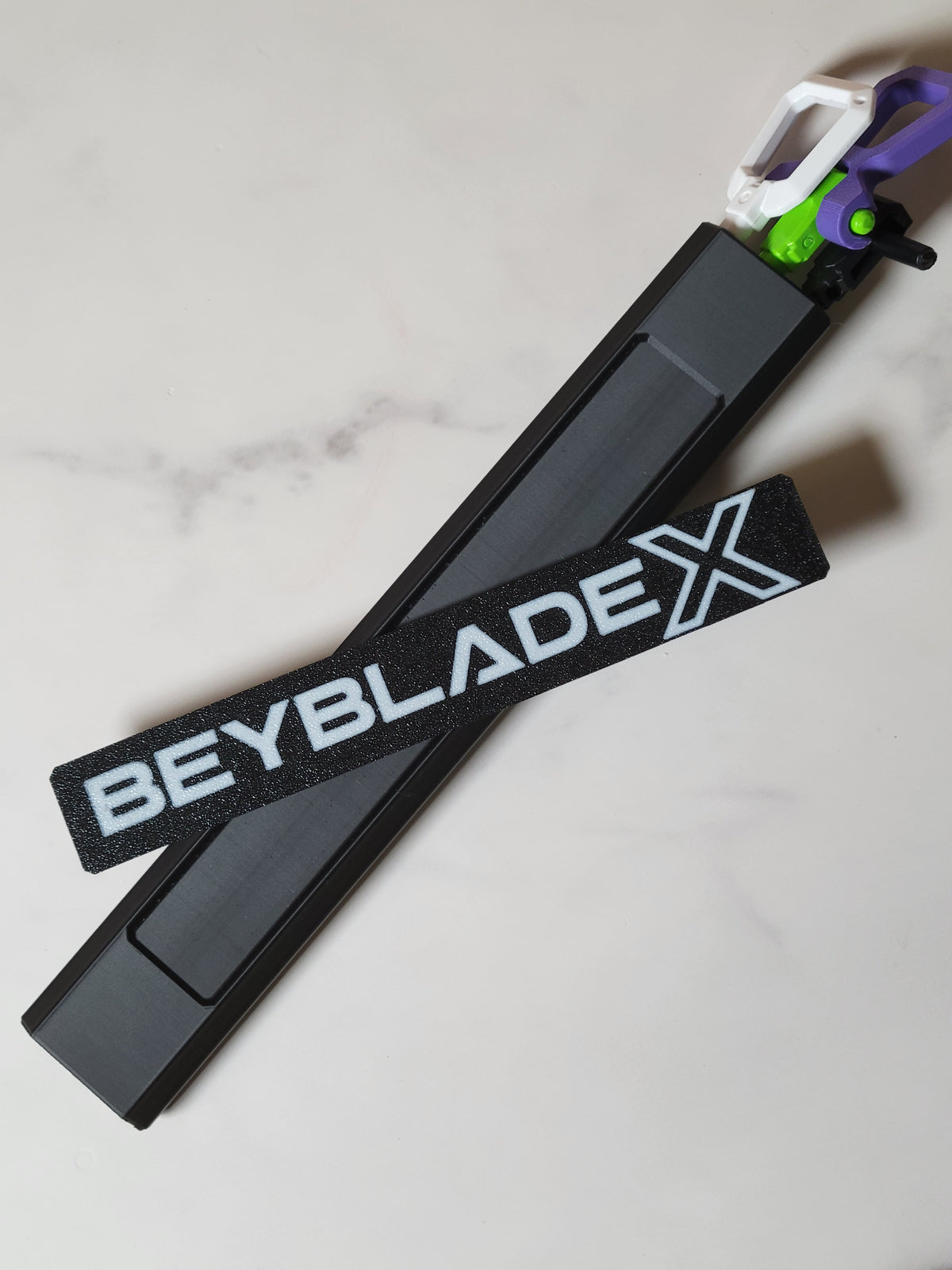 Black hex rip cord protector beside its separate white-lettered Beyblade X logo panel, with rip cords loaded.