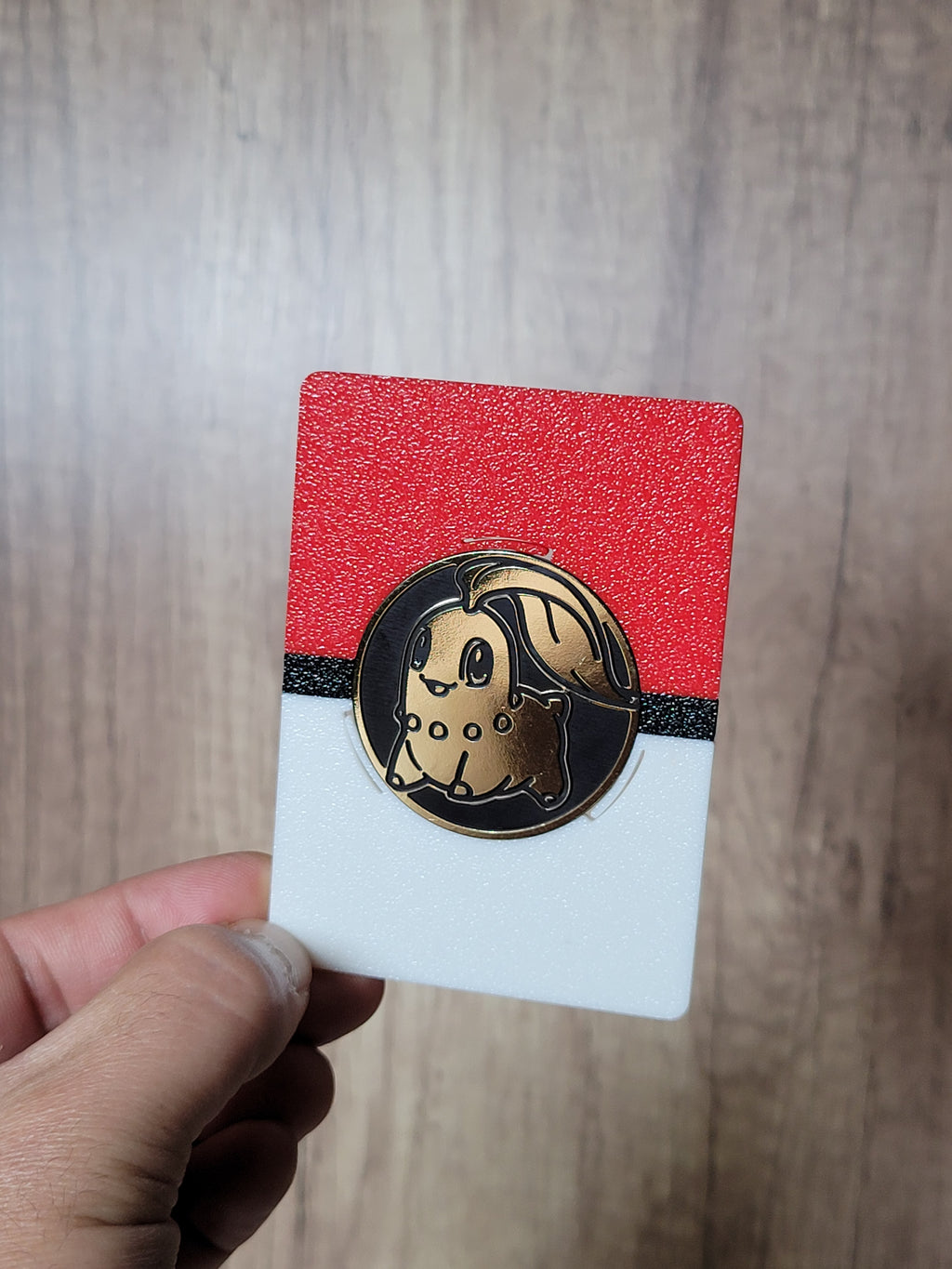 Front view of a red, black and white coin display holding a Chikorita coin, shown in one hand.