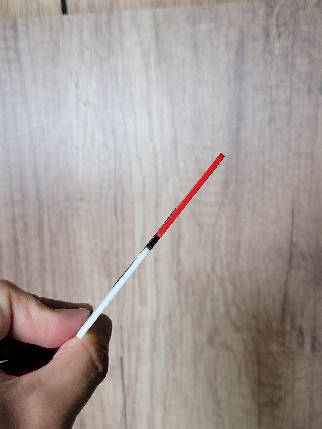 Thin edge of the red, black and white coin display held between two fingers.