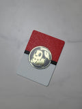 Red, black and white card-size coin display holding a gold Chikorita Pokémon coin on a light marble-patterned tabletop.