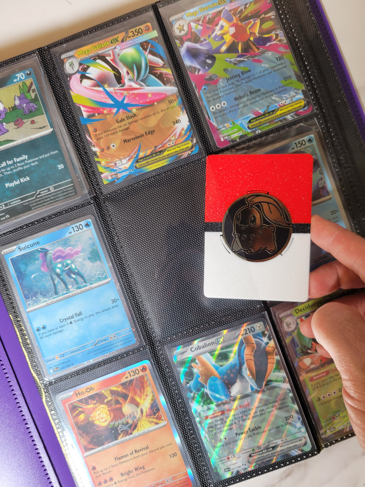 Coin display held above an open trading-card binder, with a coin centered in the frame and Pokémon cards in nearby pockets.