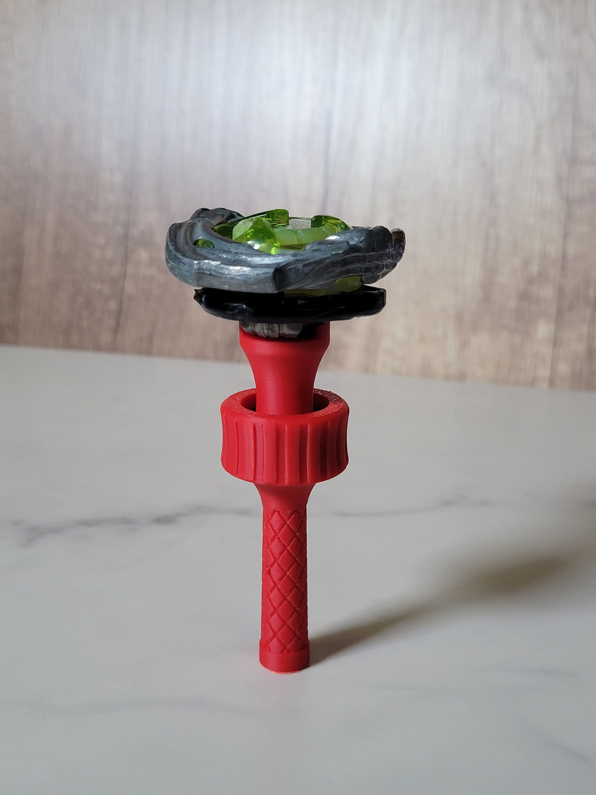 Red Beyblade X balancing tool with a blade and ratchet mounted above the bearing grip on a marble-patterned tabletop.