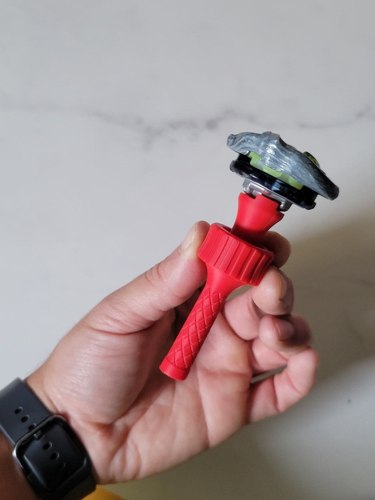 Handheld view of the red balancing tool with a Beyblade X blade and ratchet attached, showing its compact size and use.