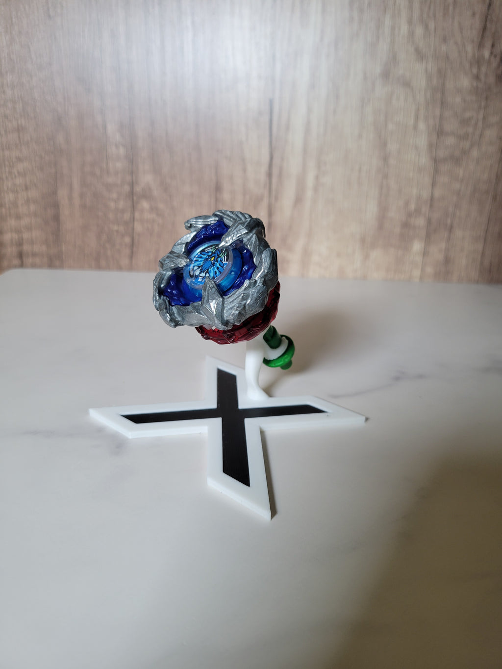 Angled front view of the split-view Beyblade X stand with the blade, ratchet and bit displayed separately.