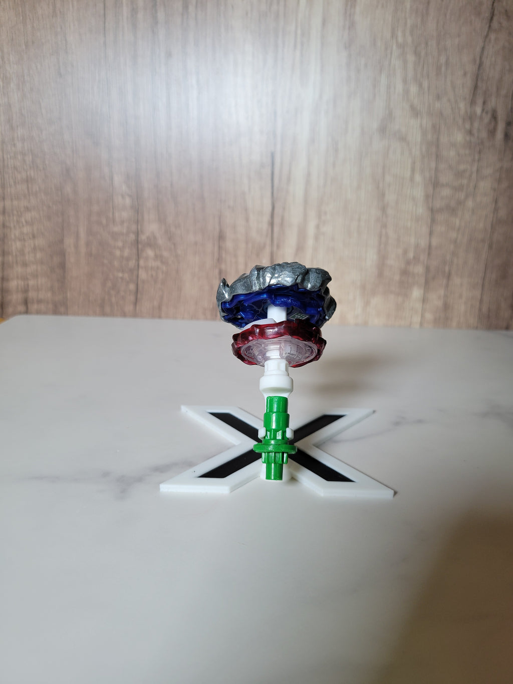 Rear view of the white-and-black X-shaped stand showing how the Beyblade parts rest in their display positions.