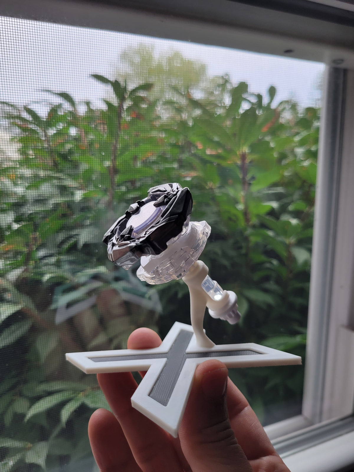 Handheld view of the split-view stand displaying a different Beyblade X blade, ratchet and bit.