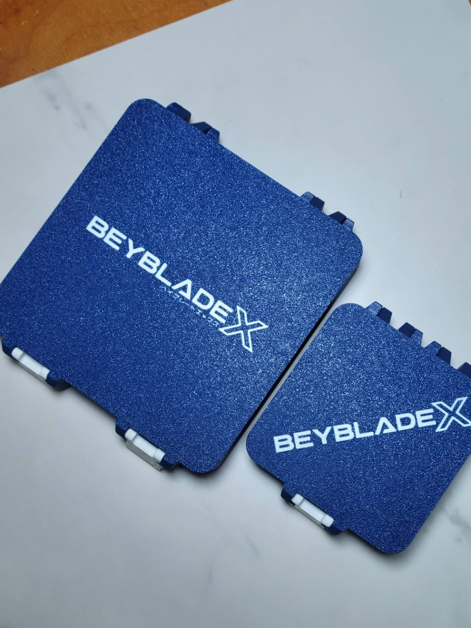 Blue and white 64-slot and 25-slot Beyblade X Bit Boxes shown side by side.