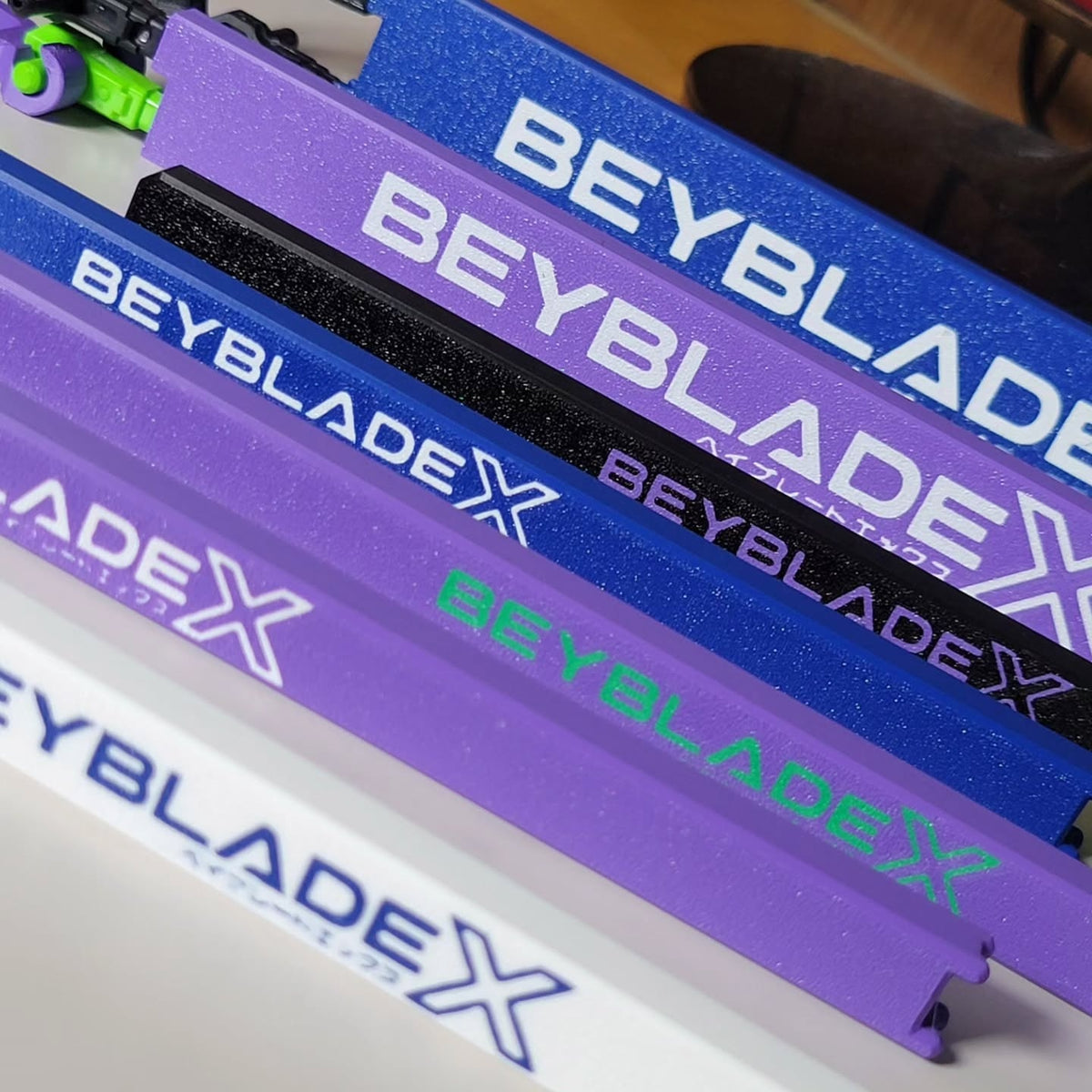 Purple, blue, white and black Beyblade X rip cord protectors with contrasting lettering.