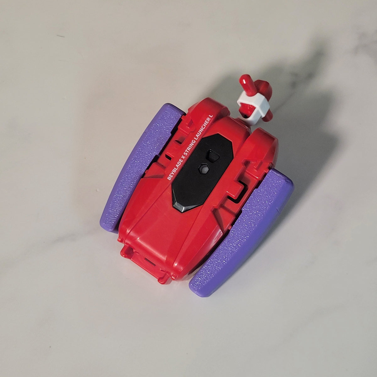 Red Beyblade X string launcher fitted into a purple Ruzz3D grip.