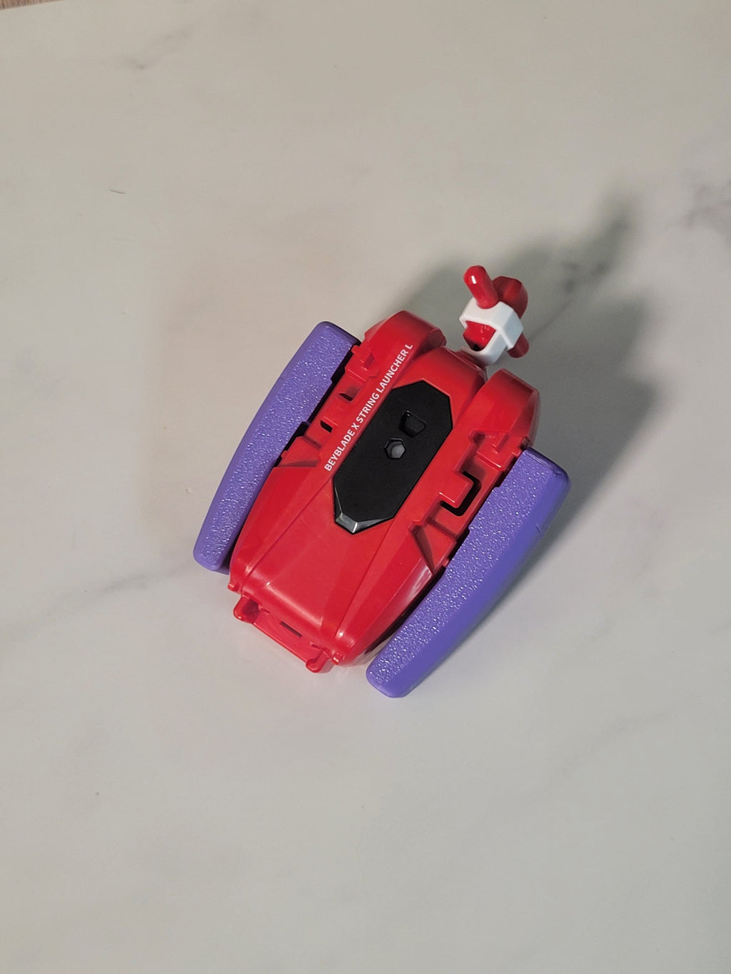 Red string launcher with a purple grip shown from the front.