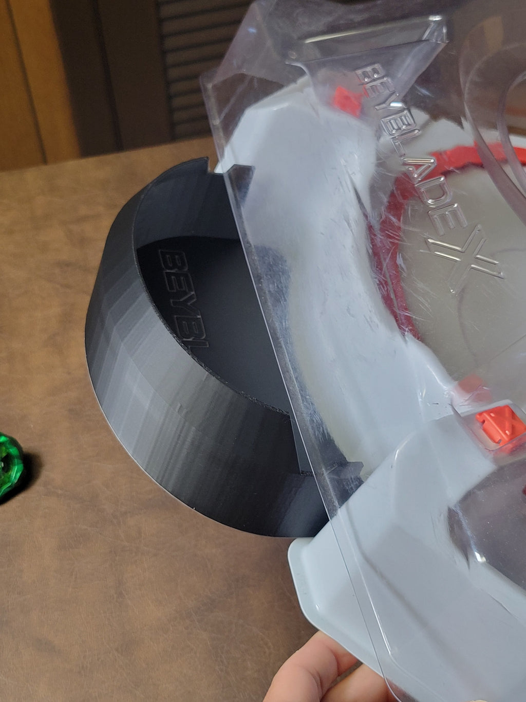 Close-up of the catch tray connection outside a clear Beyblade stadium.